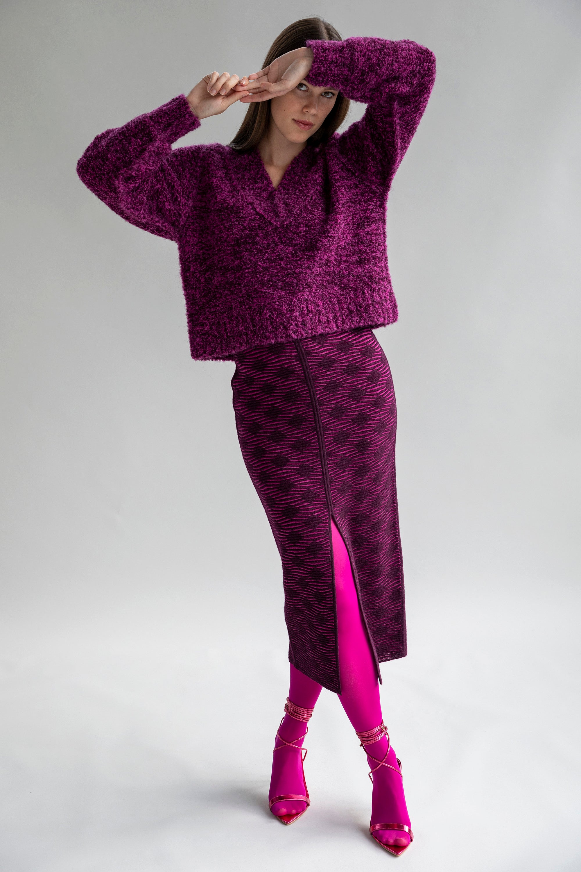 Model wearing the fuchsia aubergine Ines pencil skirt in fuchsia aubergine paired with a chunky V-Neck boucle sweater in fuchsia aubergine in a baby alpaca texture.
