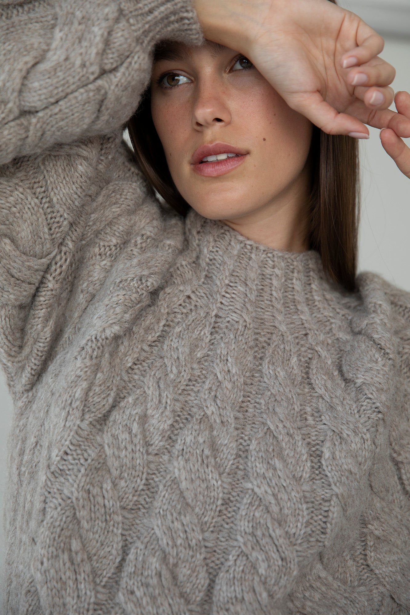 Model Amrine peeking through the sleeve of the Tomo Handknit in Oat Heather, showcasing the dramatic, fluffy texture of the sweater. The soft alpaca blend yarn creates a voluminous, cozy look.