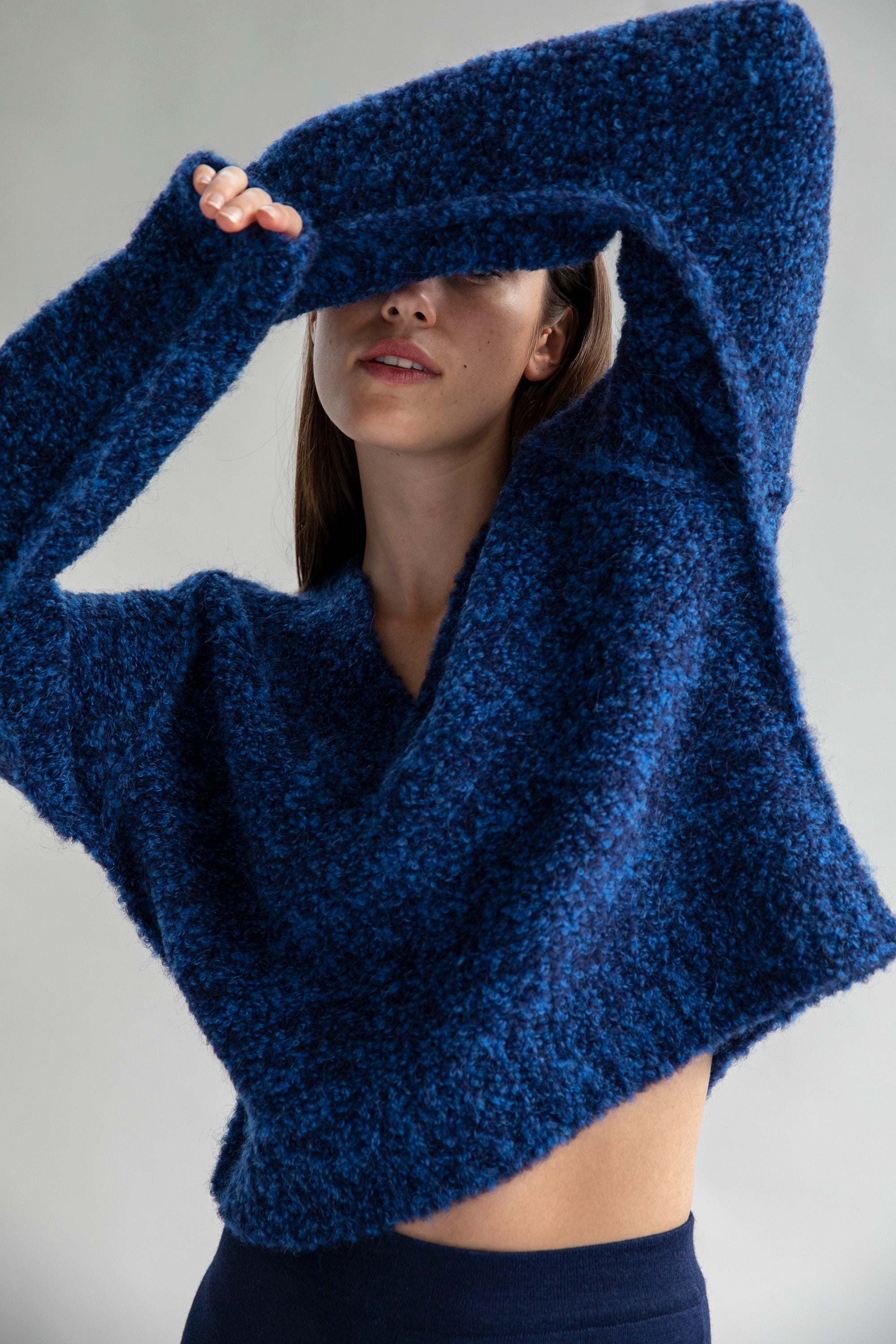 Model partially covering her face while wearing a Sky Navy sweater made from 89% superfine alpaca and 11% nylon, highlighting its cozy texture.