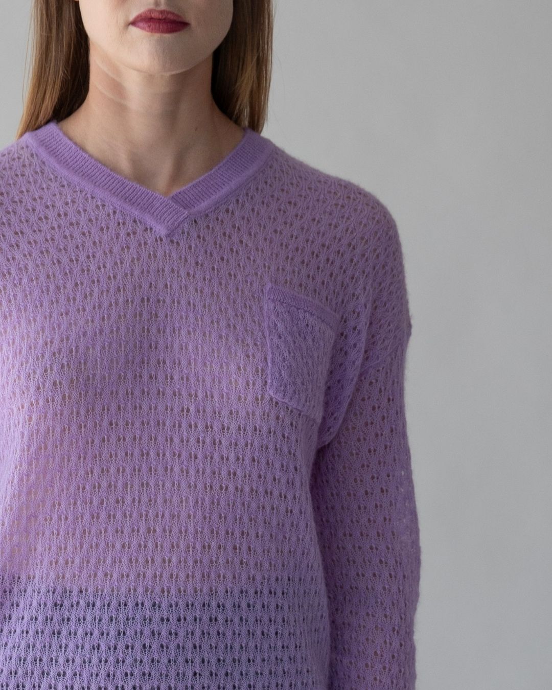 Woman wearing SSKEIN’s Lacey Iris Sweater in iris purple, featuring soft alpaca knitwear, pointelle stitching, ribbed trim, and a menswear-inspired patch pocket.