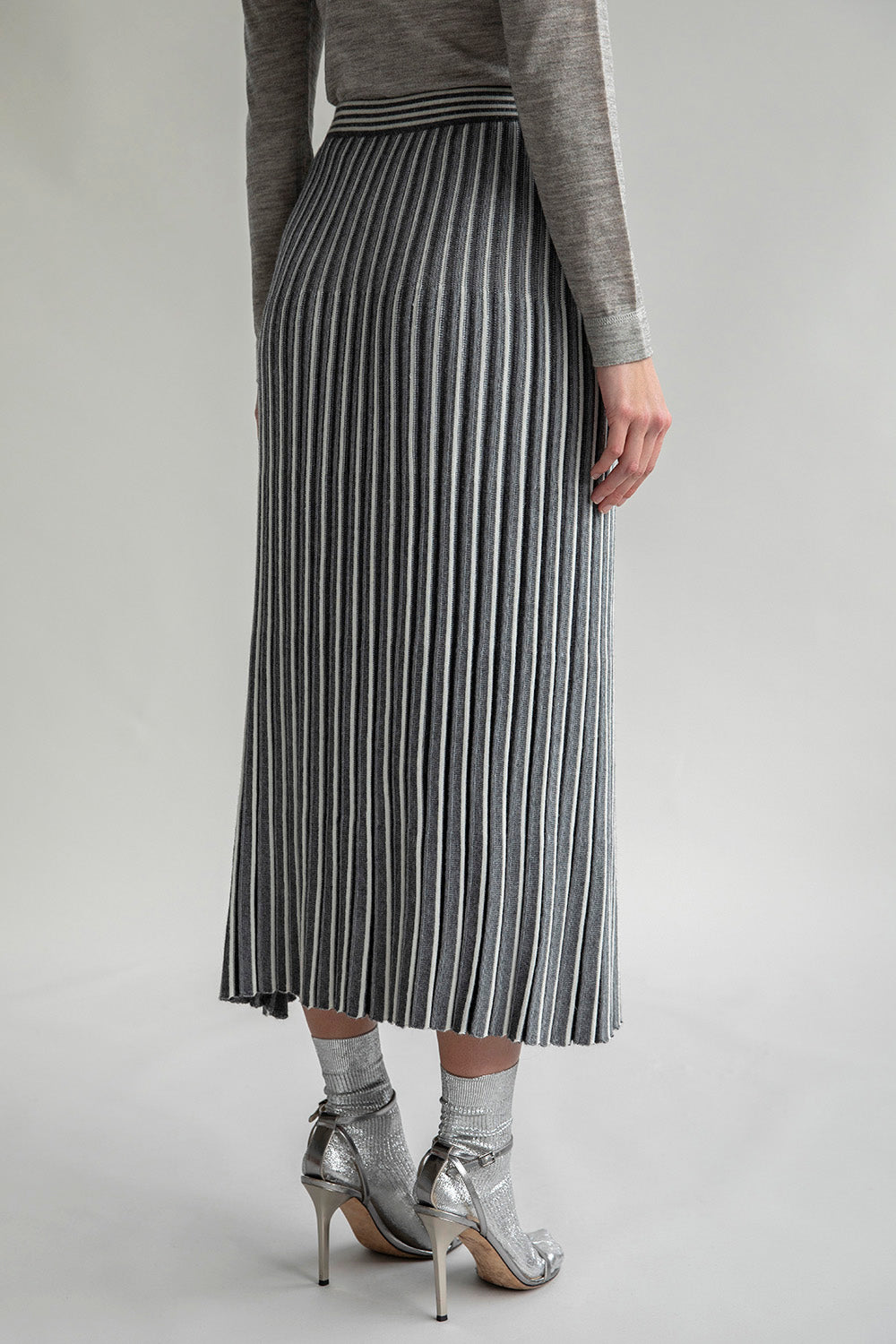 Side view of the Adeline Skirt, highlighting its versatile pleats and elegant silhouette, styled with silver socks and metallic heels.