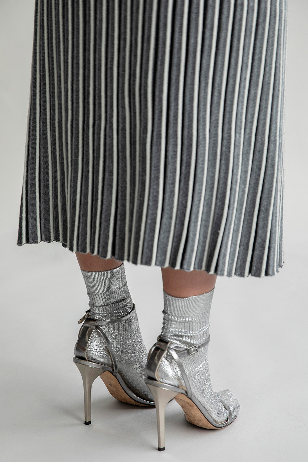 Detail shot of the bottom of the Adeline Skirt, highlighting the pleated design and contrasting stripes for a graphic finish, styled with silver socks and metallic heels.