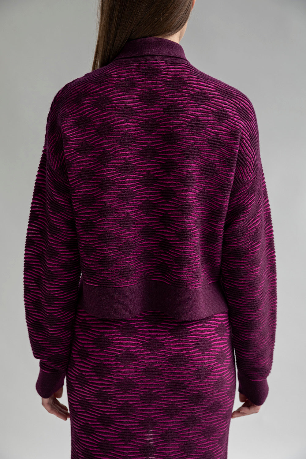 Full back view of a model wearing the Amelie Polo in fuchsia aubergine.