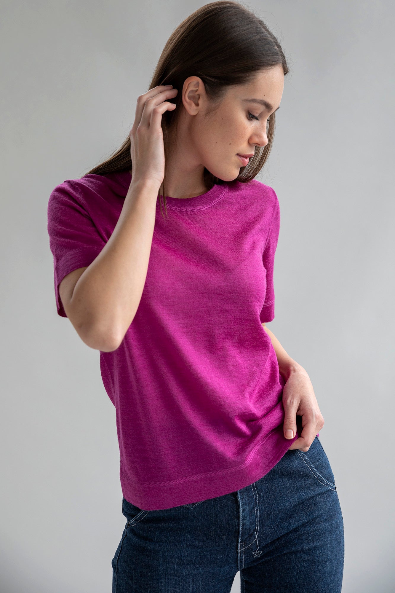 A model posing in fuchsia crew neck sweater tee made from luxury alpaca silk, paired with dark blue denim jeans.