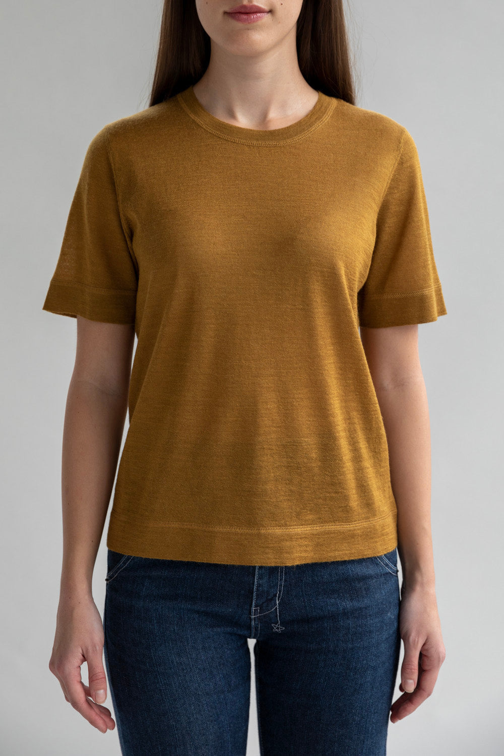 A woman wearing a golden short sleeve sweater tee made from baby alpaca silk, ethically produced in Peru.