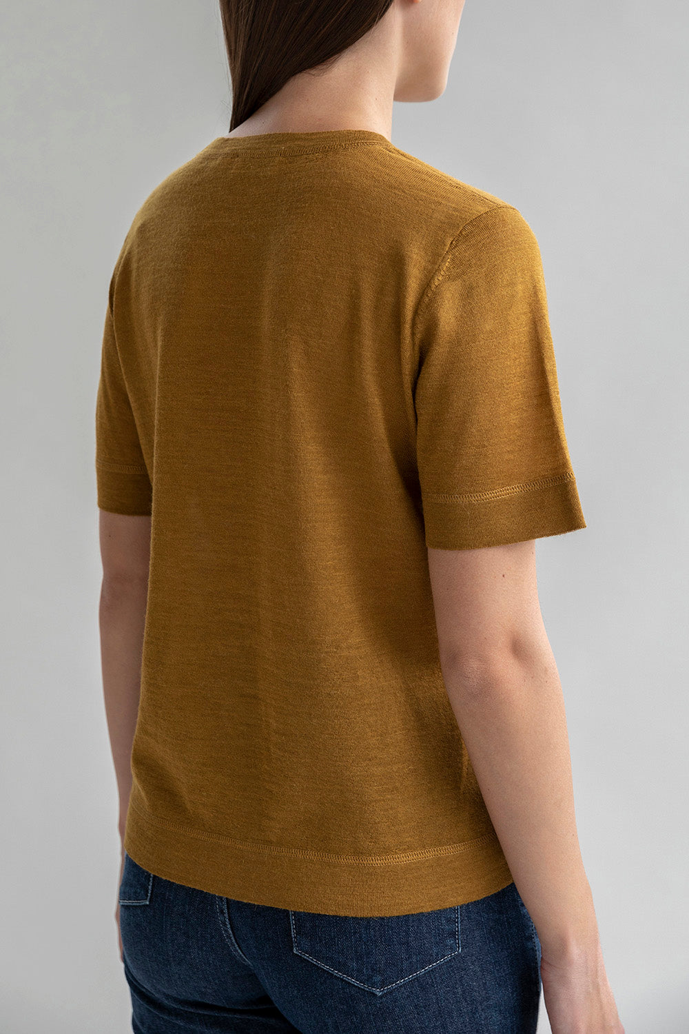 Back view of a woman wearing a golden crew neck sweater tee.