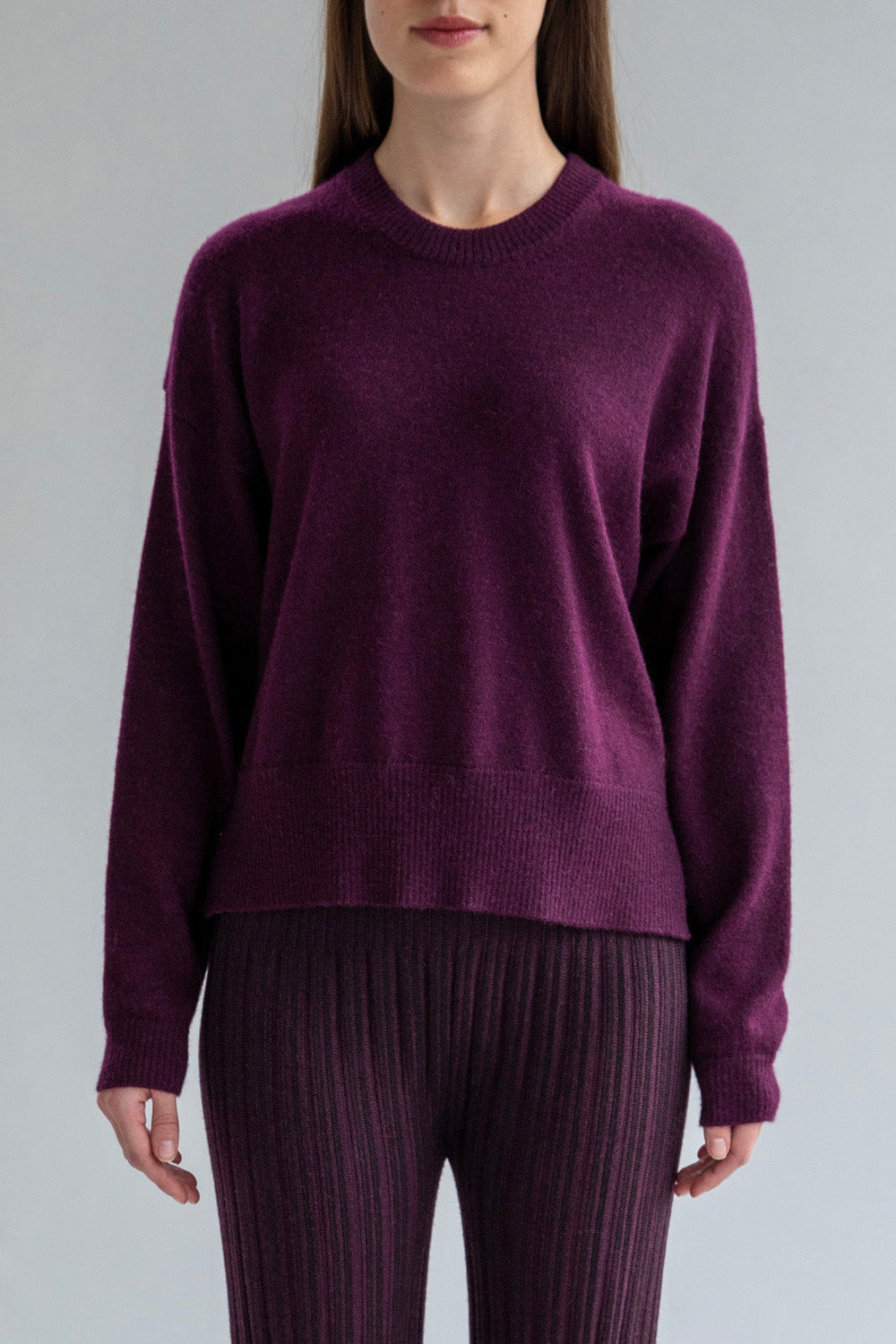 A model wearing a fitted crew neck boxy pullover in aubergine, ethically made from baby alpaca.