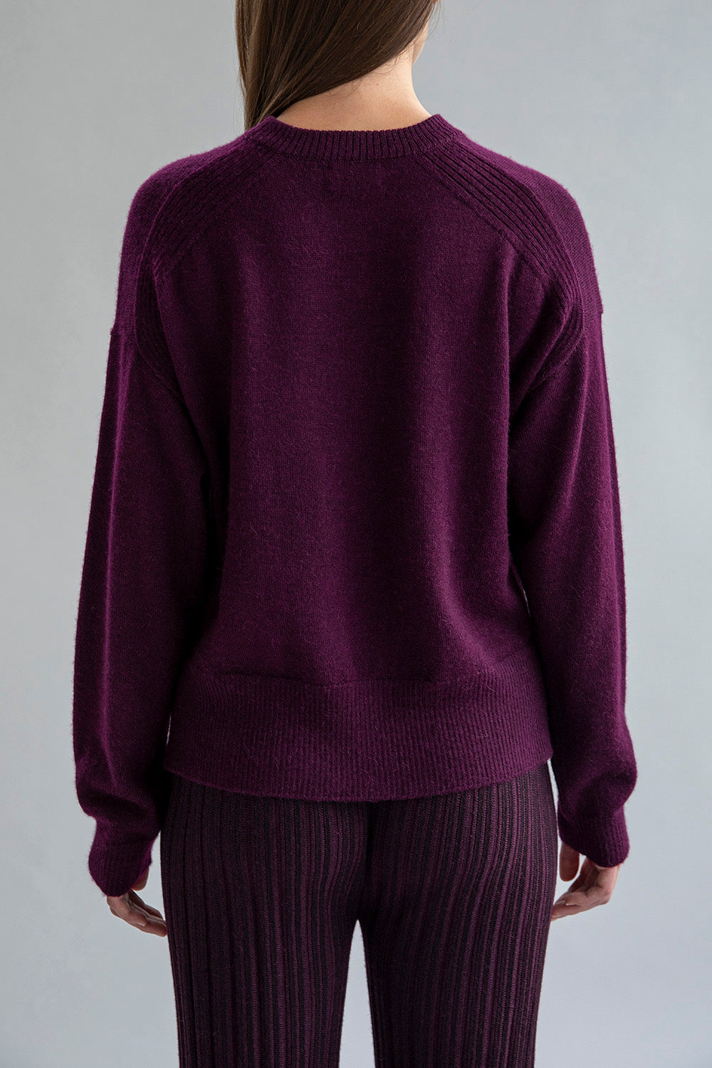 Full back view of a model wearing a crew neck alpaca sweater in aubergine.