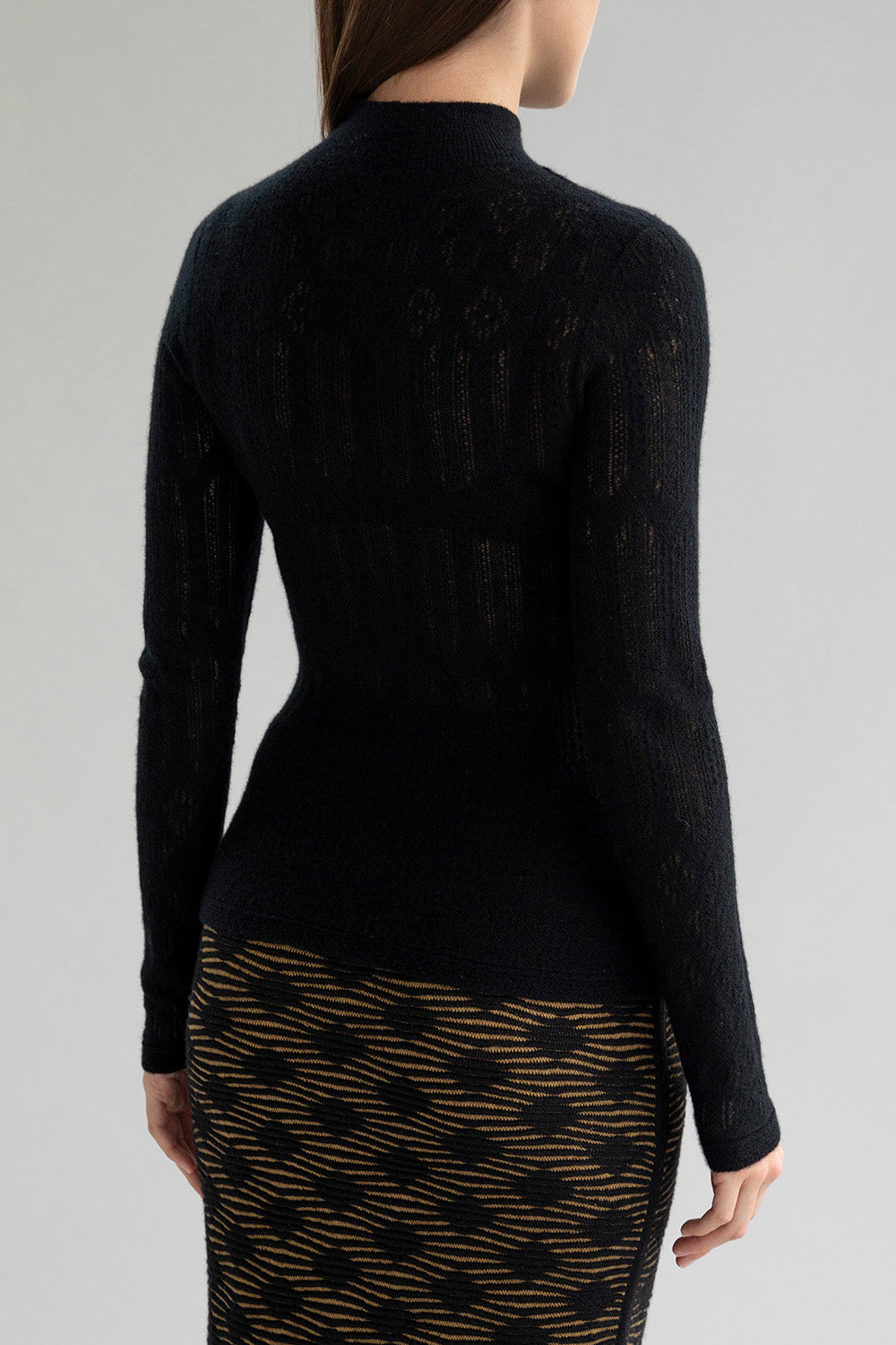 Back view of a woman wearing a lace pointelle pullover in black showcasing a fitted silhouette. 