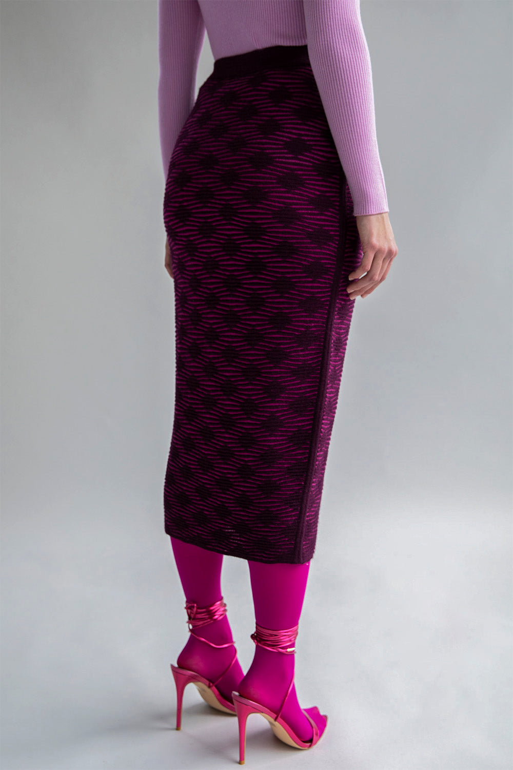 Side view of a slim-fitting fuchsia aubergine pencil skirt, featuring a subtle monochromatic pattern.