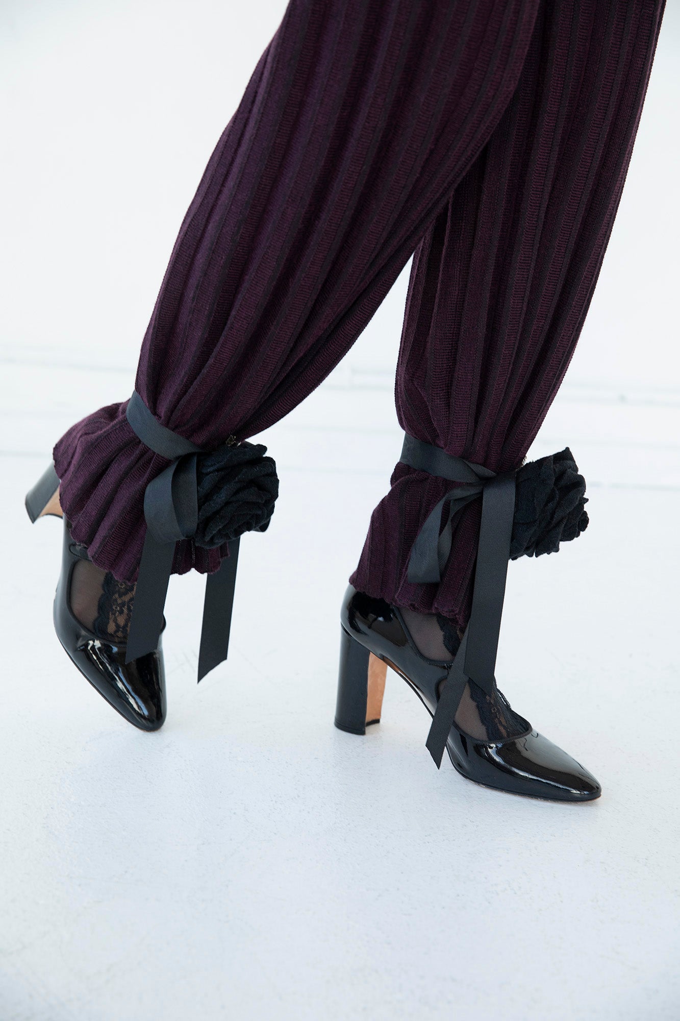 Close-up of black handcrafted up-cycled roses cinching the pant legs of the Marcelle Trousers in aubergine.