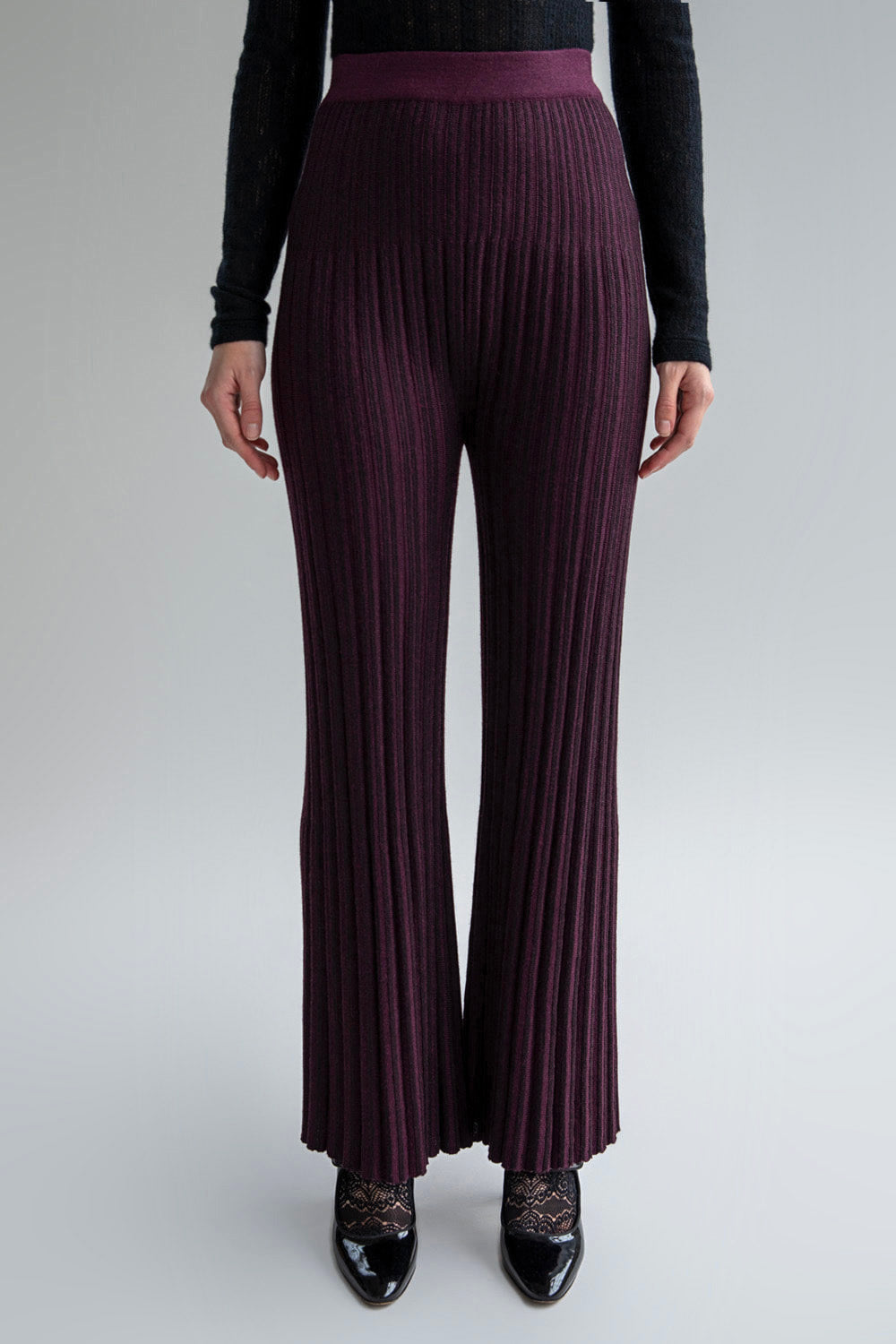 Front view of a woman wearing mid-rise aubergine trousers with a flare-leg and pleated hem effect.