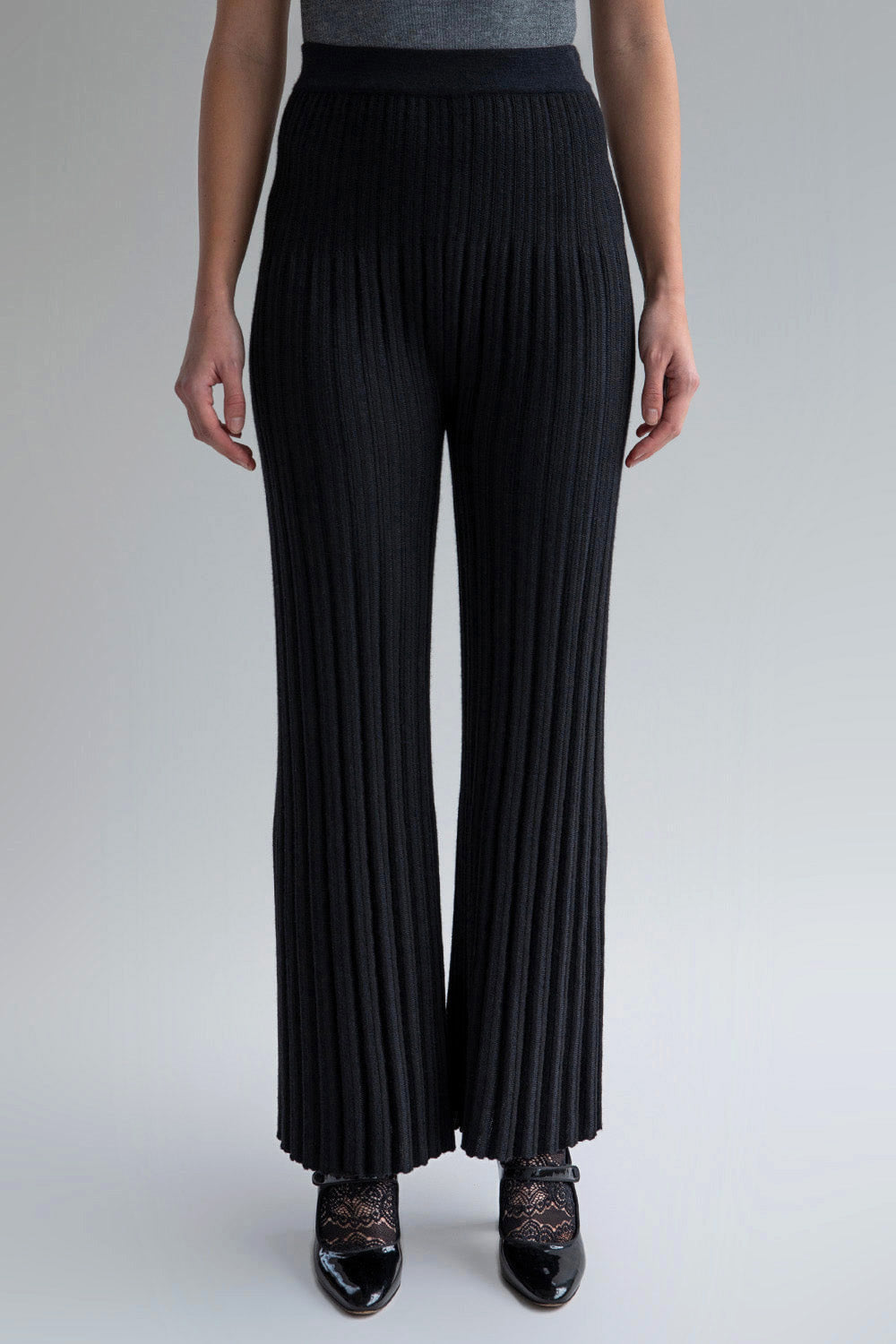 Front view of a woman wearing mid-rise black trousers with a flare-leg and pleated hem effect.