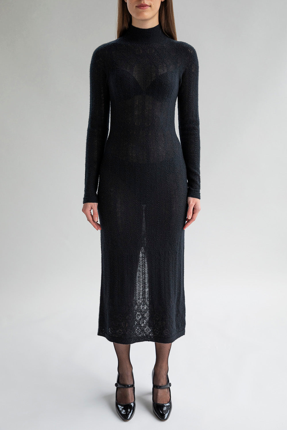 Woman wears the Margot Dress in black, featuring a lace pointelle pattern in soft cashmere showcasing a fitted silhouette.