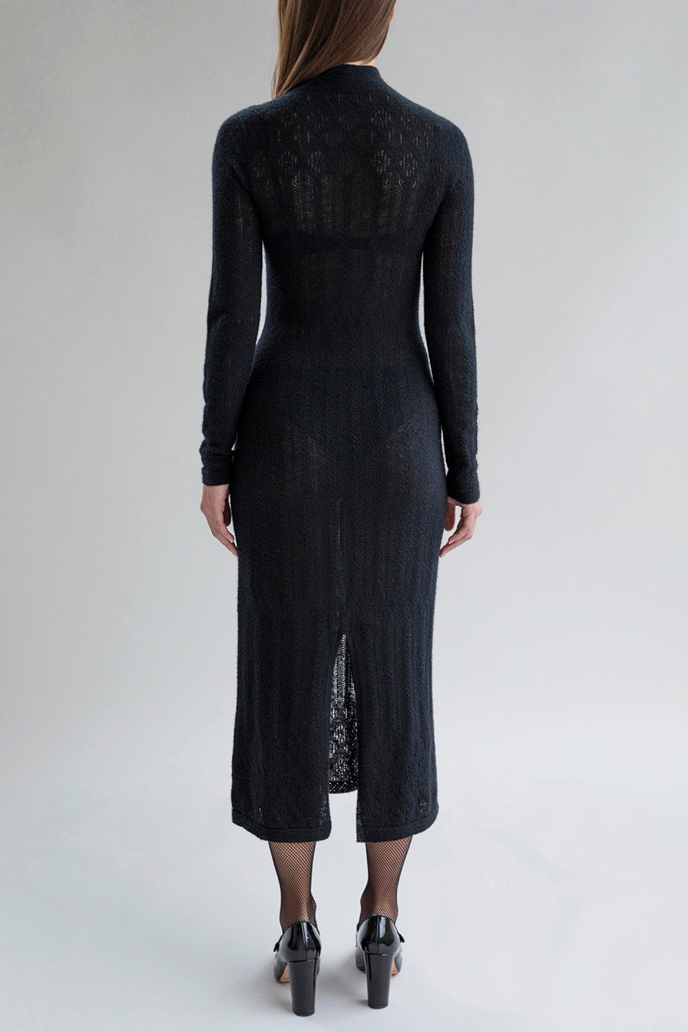 Full back view of a woman wearing the Margot Dress, featuring a sheer lace pointelle design, turtleneck top, mock neck sleeves, and a center back slit for ease of movement.