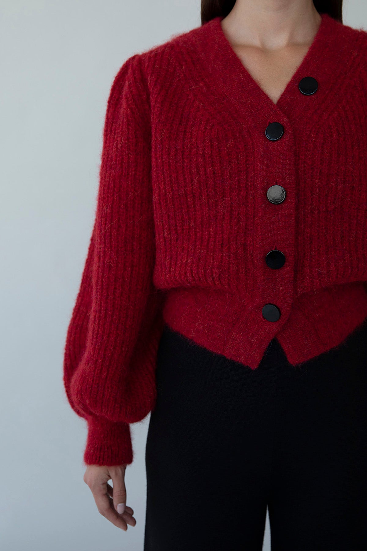 Close-up of the cardigan's front buttons, featuring four vertical black buttons and a unique asymmetrical fifth button for added detail and play.