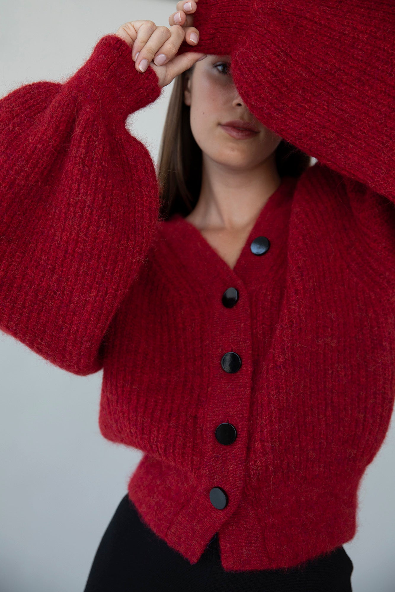 Model in the MP Cardigan in crimson red, raising her arms and peeking through the dramatic, oversized sleeves. 