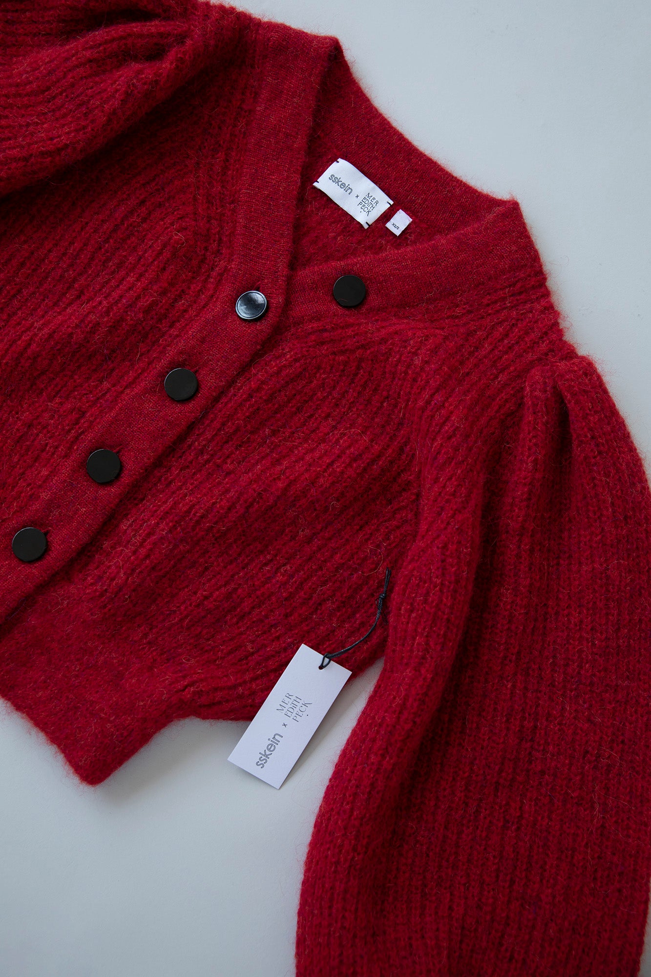 Flatlay of the MP Cardigan in crimson red, showcasing its sleek design, black button details, and feminine silhouette.