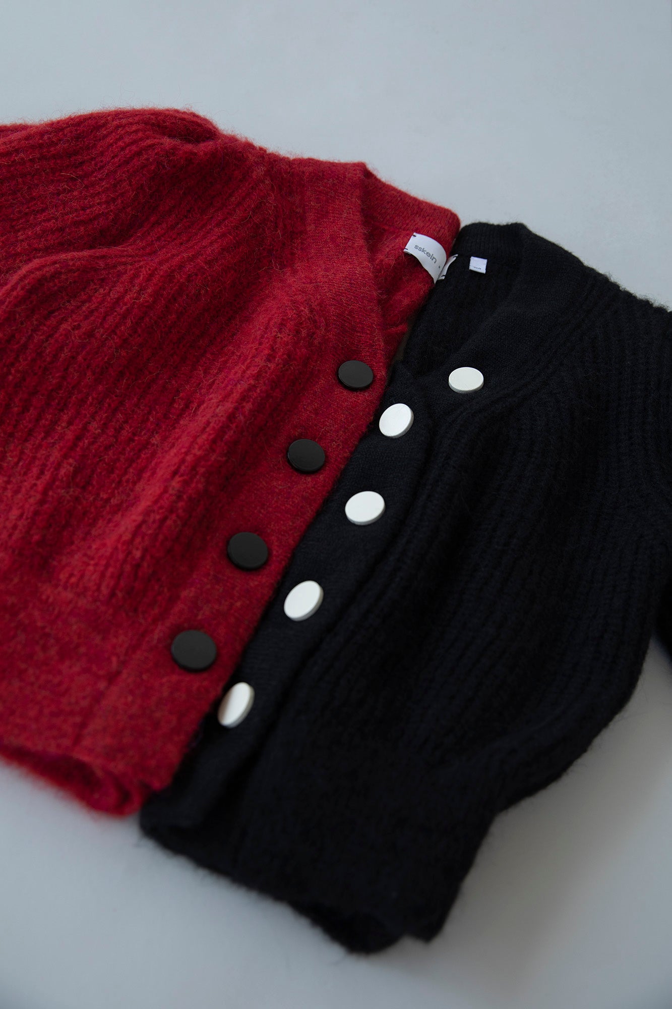 Flatlay of the MP Cardigans in crimson red and black, showing the difference in button colors—white buttons on the black cardigan and black buttons on the red cardigan.