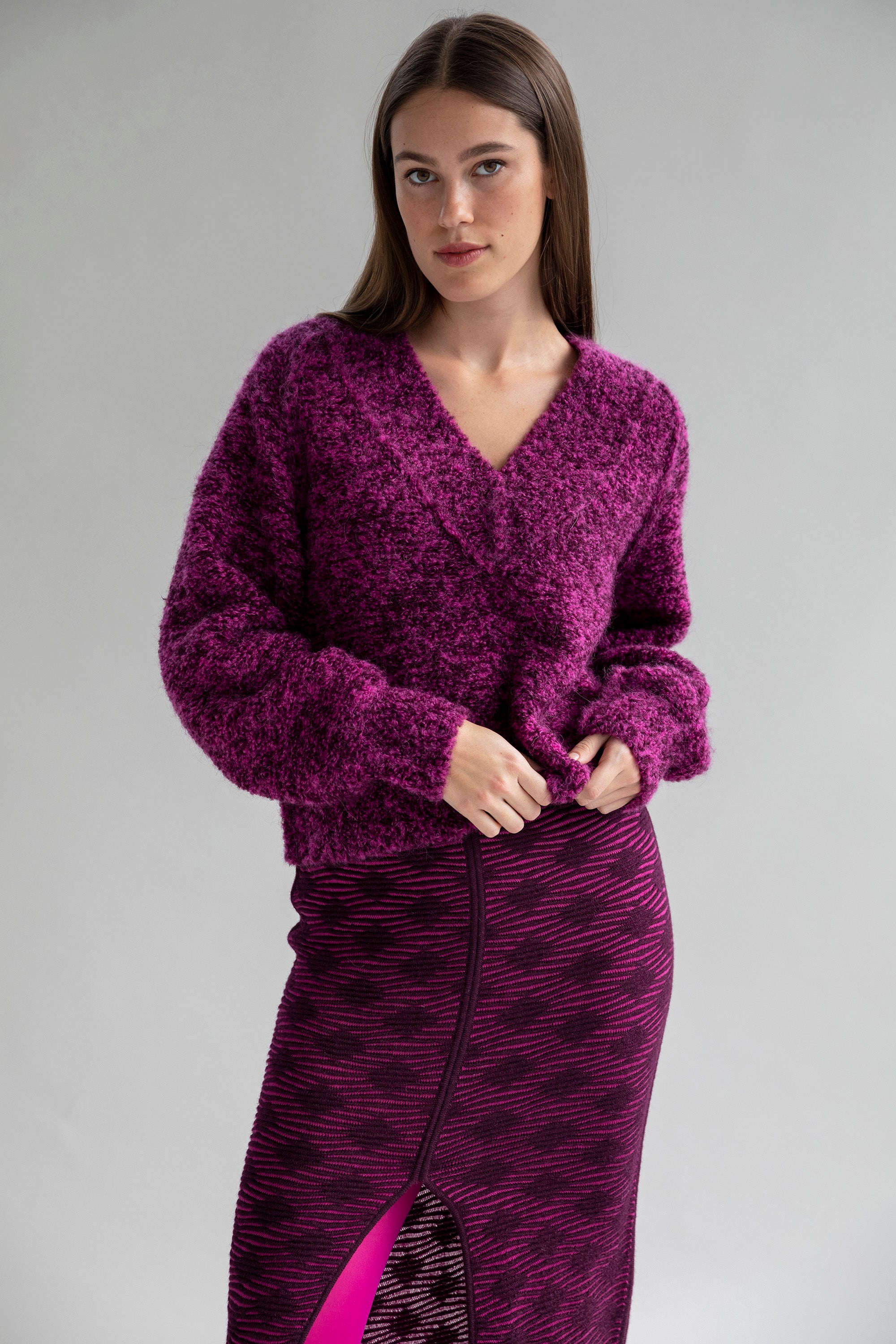 A V-neck boucle pullover sweater in deep aubergine and fuchsia, worn by a model and paired with a matching alpaca cotton blend skirt.