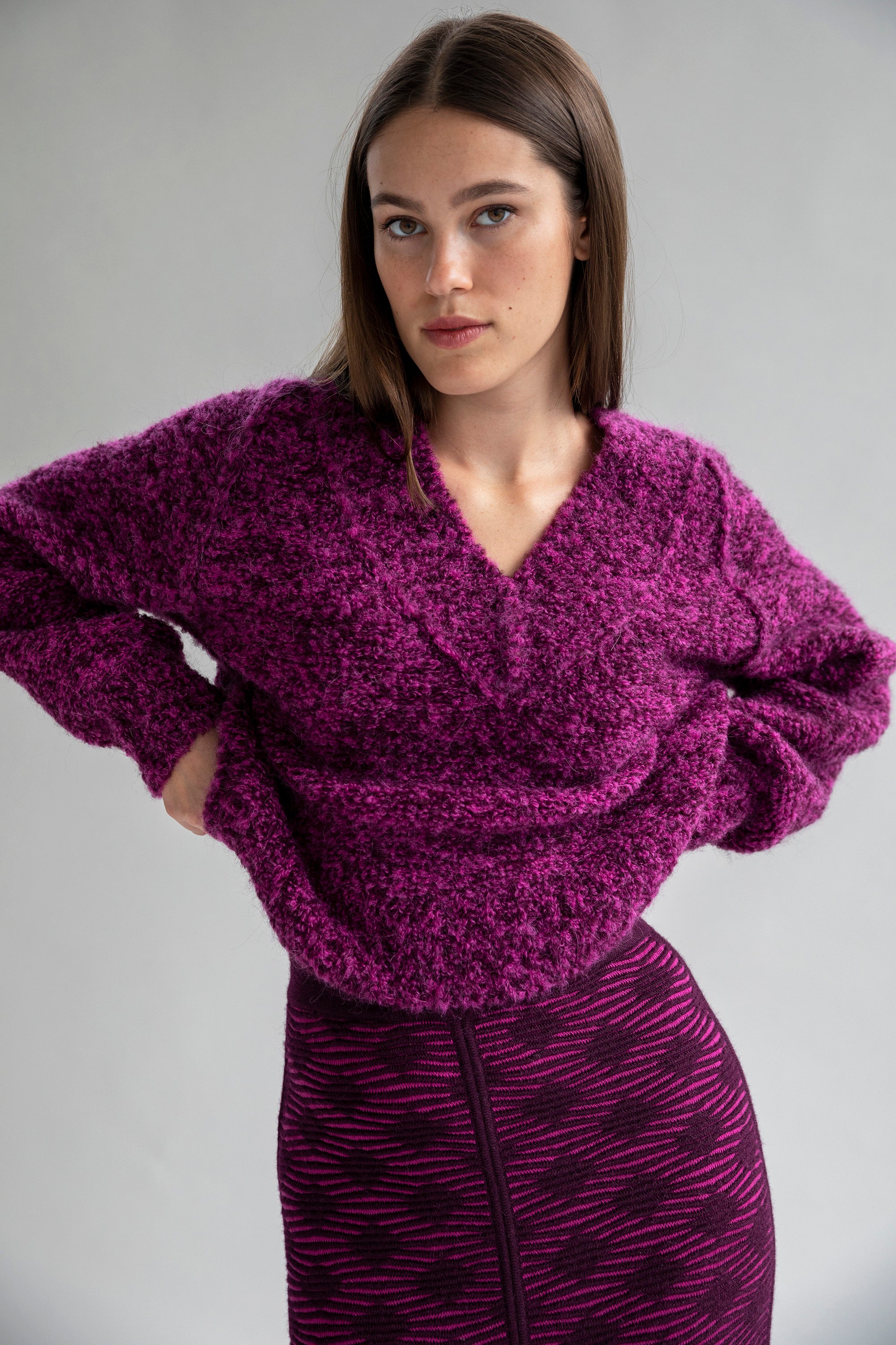 A brunette model posing in a fuchsia and aubergine V-neck boucle pullover sweater, ethically made from superfine alpaca.