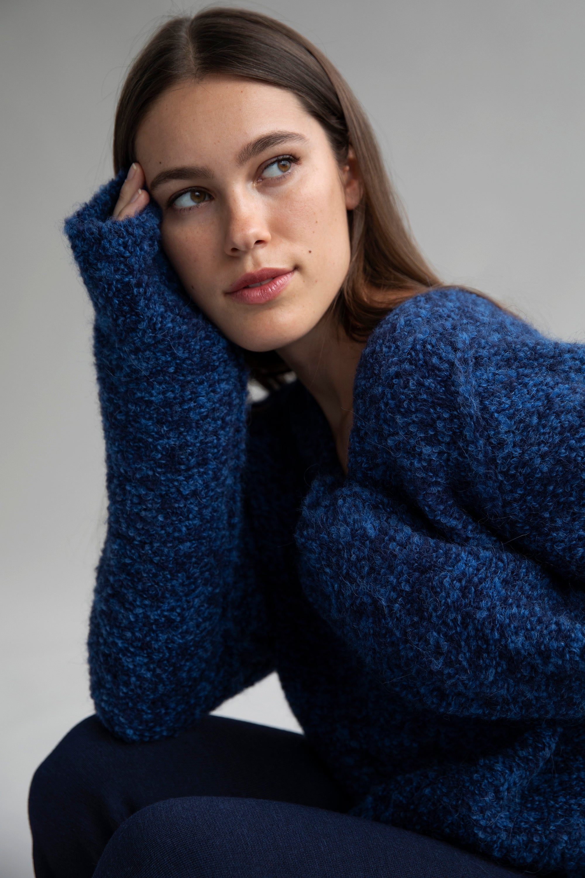 A brunette model posing in a Sky Navy blue V-neck bouclé pullover sweater, ethically made from superfine alpaca.