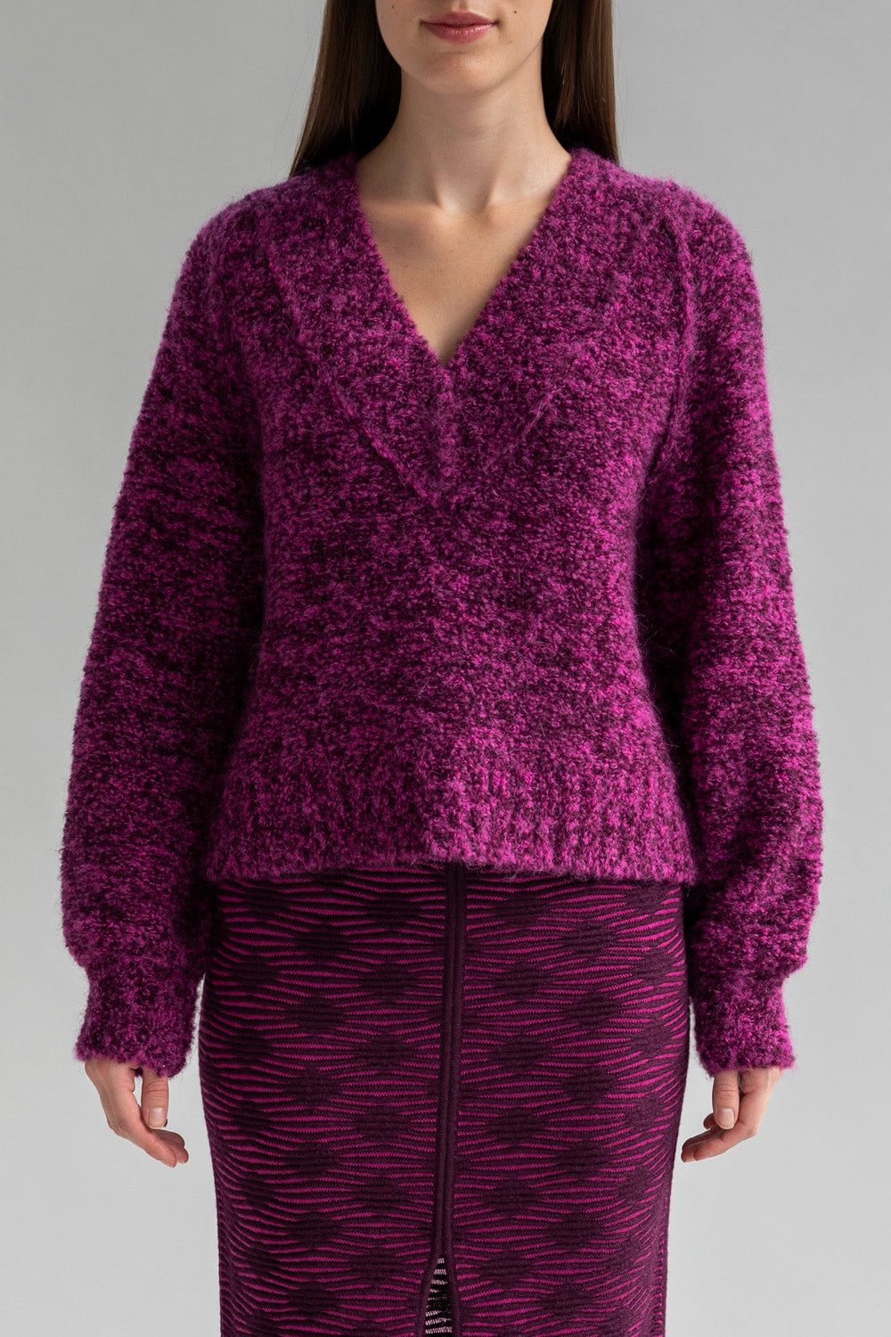 A woman wearing a chunky fuchsia colored long sleeve V-neck sweater made from superfine alpaca.