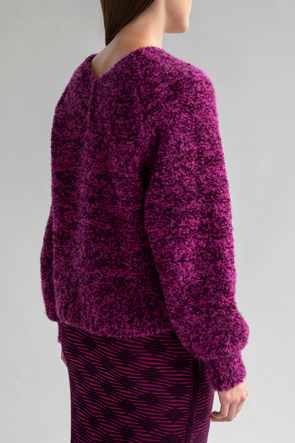 Back view of a woman wearing a boucle sweater with a low V-neck in the back.