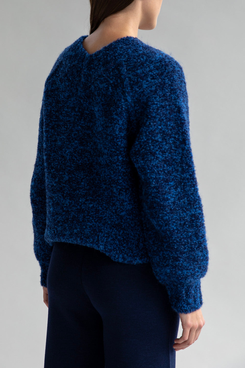 Back view of a woman wearing a boucle sweater with a low V-neck in the back.