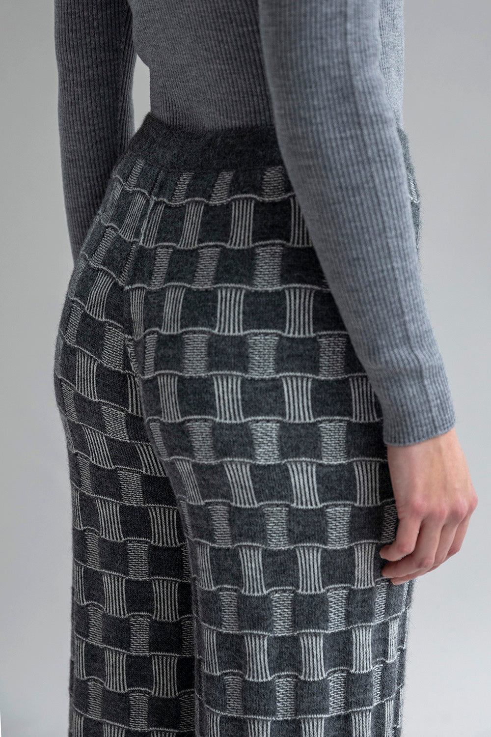 Close-up shot of Zoe Alpaca Trousers, highlighting the graphic-checked jacquard pattern in dark grey palette and the soft blend of 62% baby alpaca and 38% Pima cotton.