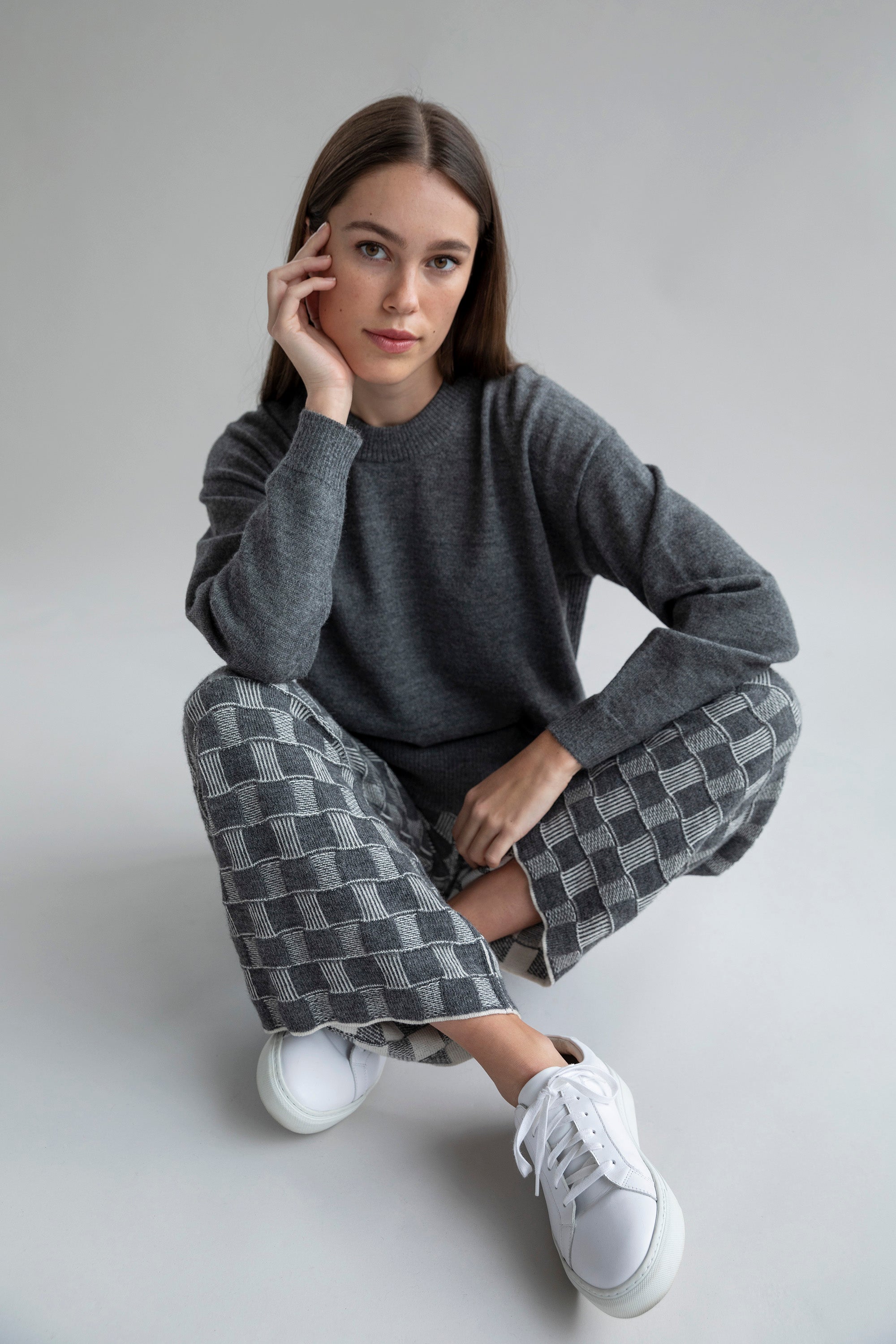 Model wearing Zoe Alpaca Cotton Knit Trousers in the darker colorway, paired with a matching grey crewneck boxy pullover and white Veja sneakers for a casual look.